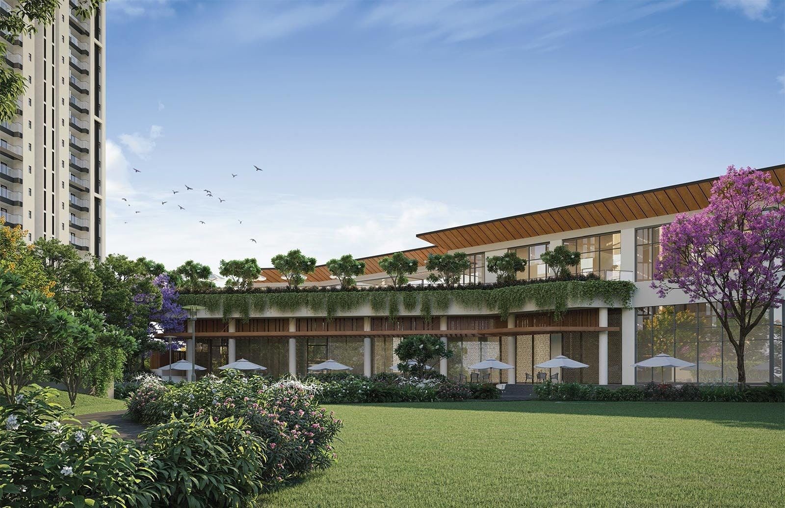 Low clubhouse pavilion beside a lawn and flowering tree, with towers behind.